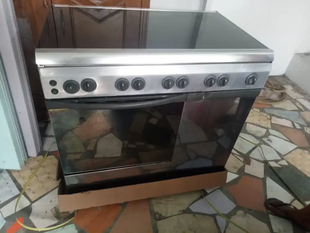 kompor gas freestanding merek Ariston dengan penutup kaca atas.