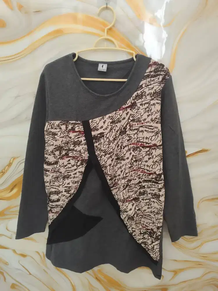 Baju atasan wanita dengan potongan asimetris dan motif tulisan.